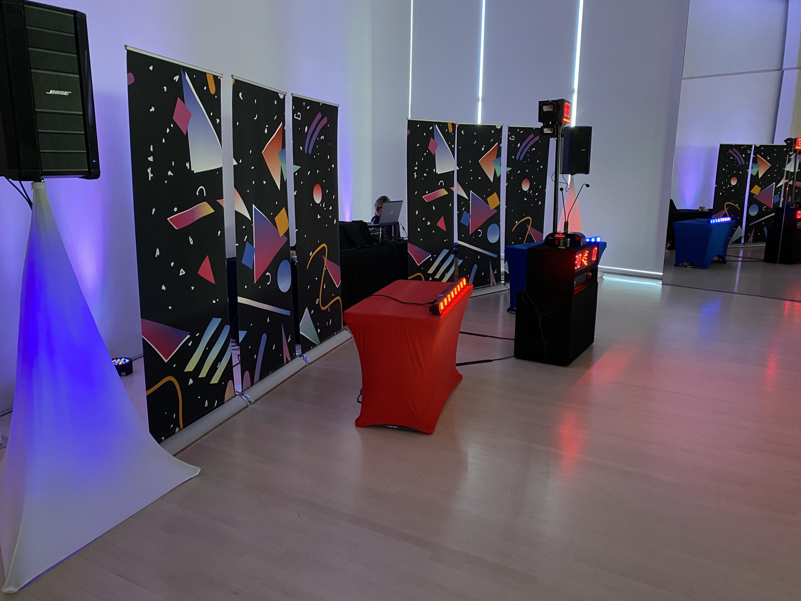 Event space setup featuring colorful banners, sound equipment, and illuminated tables, creating a vibrant atmosphere for a gathering.